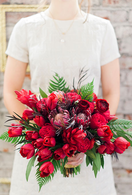 Red bouquet of garden roses, tulips, protea, and ferns